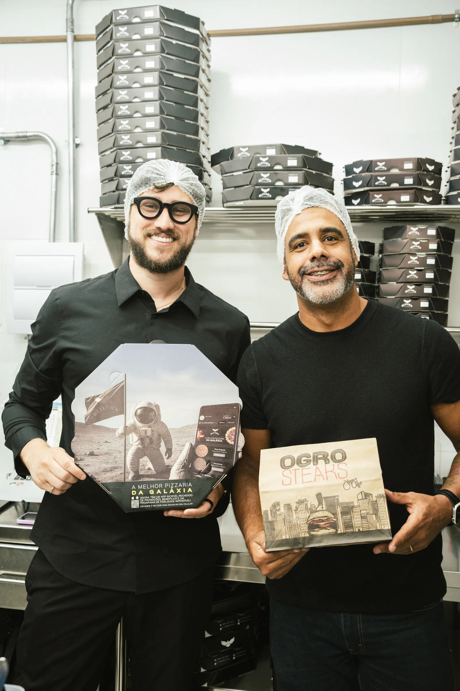Dois integrantes do grupo segurando embalagens de duas marcas diferentes na mesma cozinha